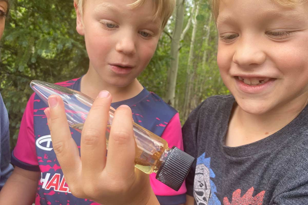 Two day camp boys look at a vial of test water from the stream