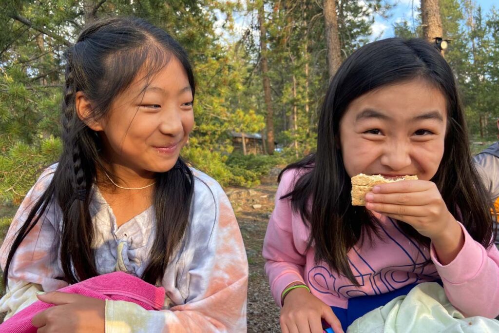 Two Discovery Campers laugh and eat s'mores at the weekly Campfire