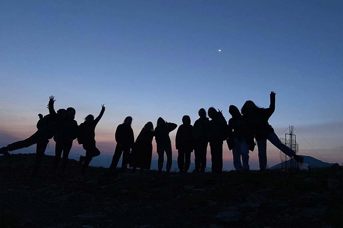 A silhouette of a group of campers on a mountain at sunrise.
