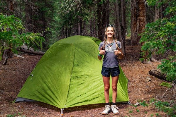 A girl finishes putting up her tent during a camping trip in the forest.