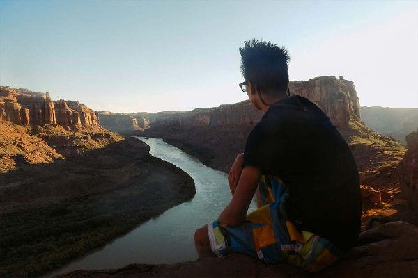 A boy looks down the the river and canyon during sunset.