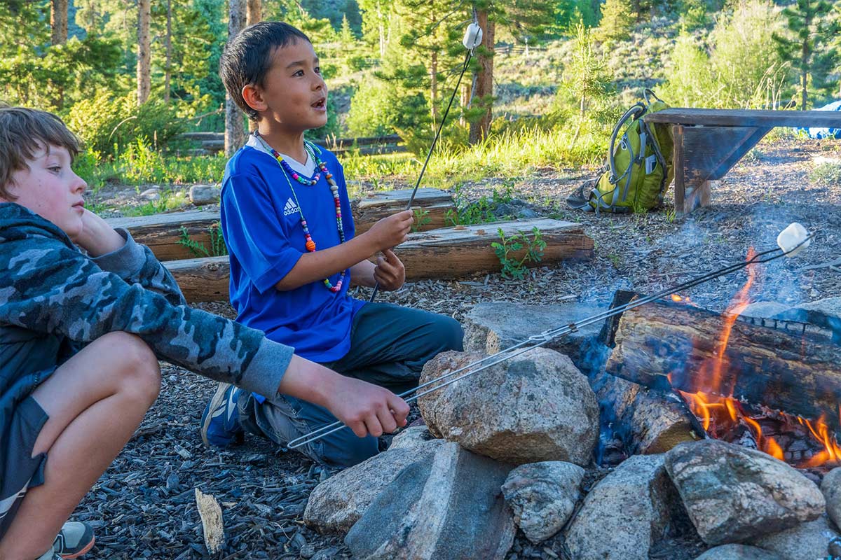 Two Discovery Campers roast marshmallows over a campfire.